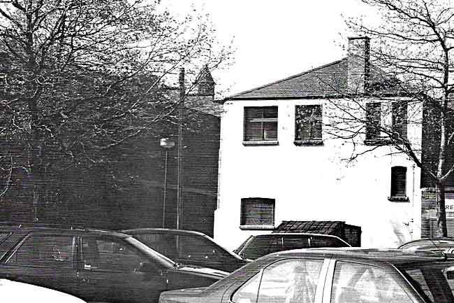 A 1997 photograph of the location painted by Annie Laurie Gilbert in 1920. The turret on the Trivett Square warehouse is the only feature to have survived the intervening years and the change from recreation ground to car park.